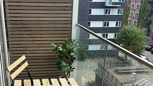 A balcony with a wooden table and chairs, a potted plant, and a view of the street below. - Light and spacious flat with balcony in Copenhagen (København S)