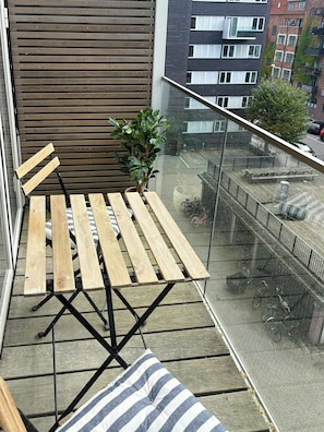 A balcony with a wooden table and chairs, a potted plant, and a view of the street below. - Light and spacious flat with balcony in Copenhagen (København S)