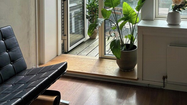 A room with a sliding glass door leading to a balcony, a black leather chair, a potted plant, and a radiator. - Light and spacious flat with balcony in Copenhagen (København S)