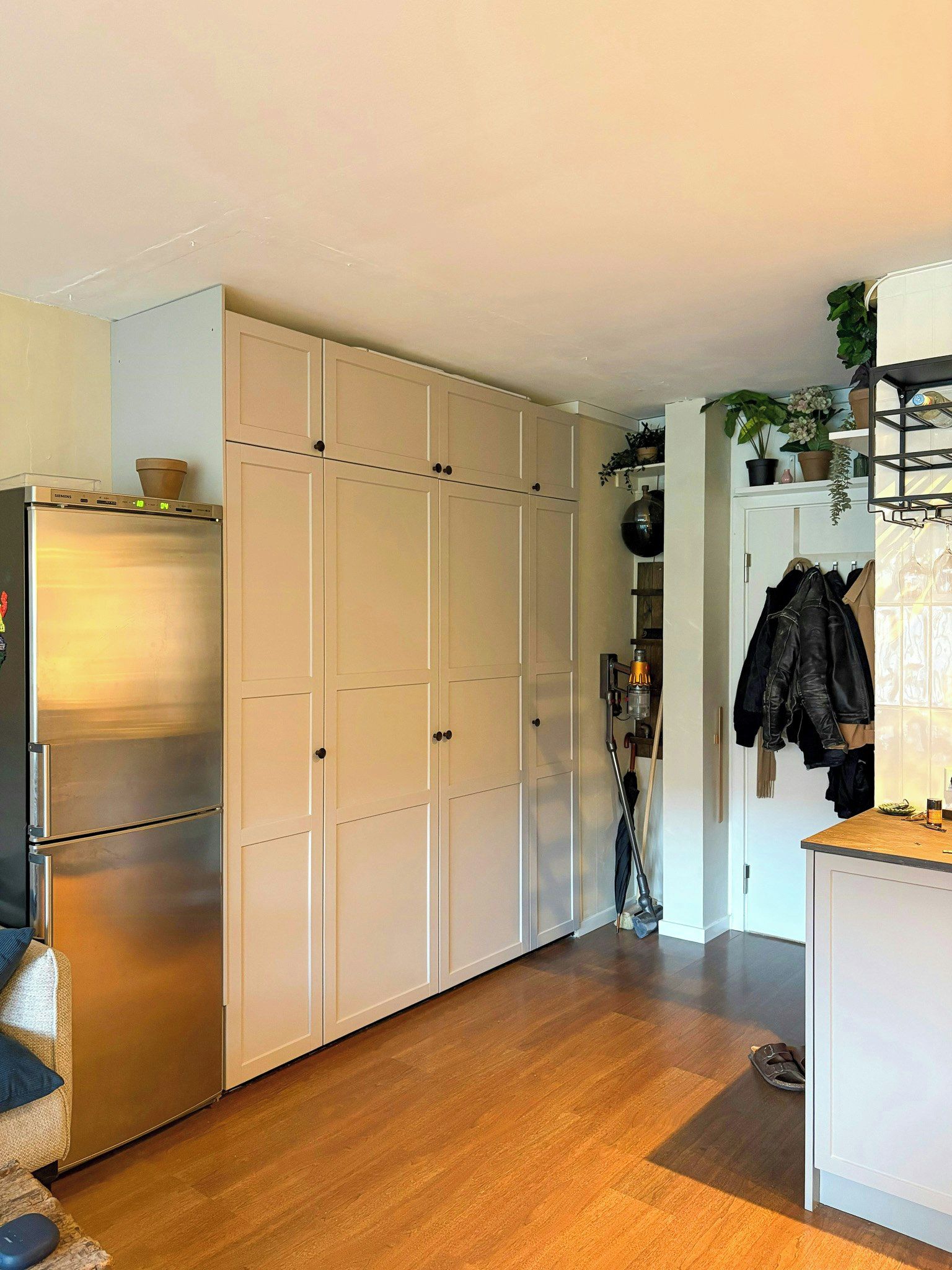 A compact kitchen with a built-in refrigerator, white cabinets, and a wooden floor.