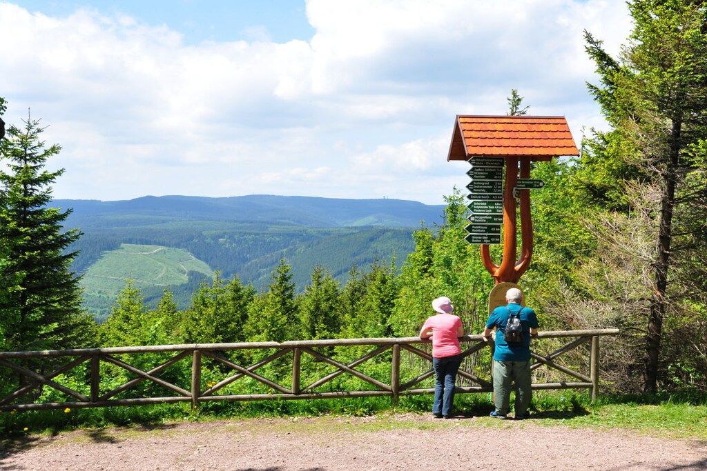 A wooden observation post with a signpost, surrounded by a wooden fence, overlooking a mountainous landscape.
