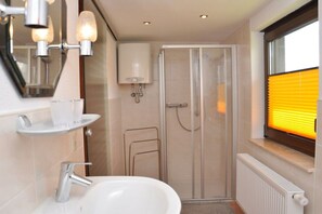 A modern bathroom with a glass shower enclosure, a white sink, and a window with blinds. - Holiday home with 1 bedroom (Frauenwald)
