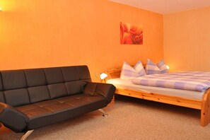 Ein Zimmer mit einer Couch, einem Bett mit kariertem Überwurf und einem Wandbild.