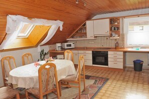 A cozy kitchen with a dining area, wooden ceiling, and a window with curtains. - Holiday apartment with 2 bedrooms (Egloffstein)