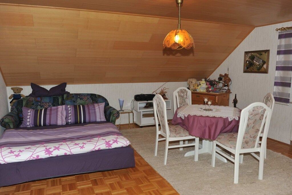 A bedroom with a sloped ceiling, a bed with patterned bedding, a desk with a chair, and a hanging light fixture.