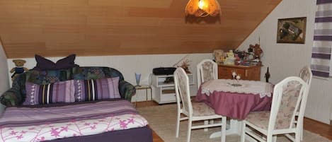 A bedroom with a sloped ceiling, a bed with patterned bedding, a desk with a chair, and a hanging light fixture.