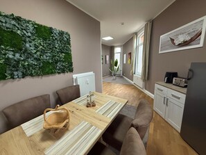 A modern dining area with a long wooden table, cushioned chairs, a woven basket, and a wall-mounted green plant. - Apartment '3' with Wi-Fi (Erfurt)