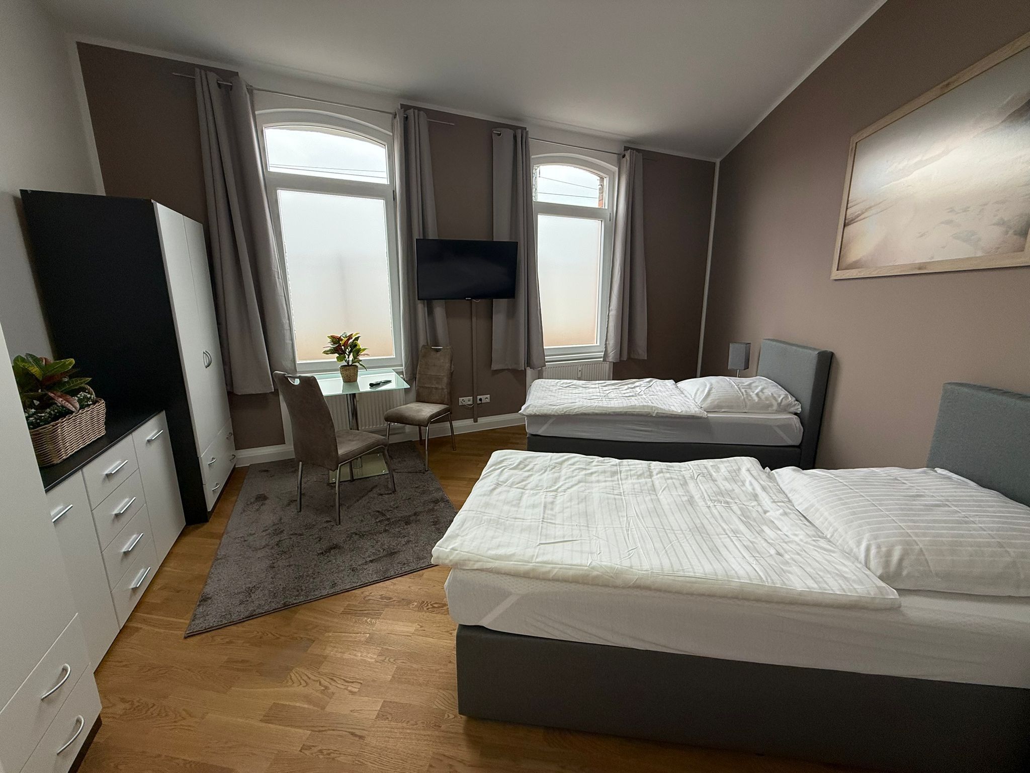 Ein Hotelzimmer mit zwei Betten, einem Schreibtisch, einem Fernseher und einem Vorhangfenster.