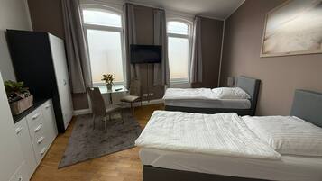 Ein Hotelzimmer mit zwei Betten, einem Schreibtisch, einem Fernseher und einem Vorhangfenster.
