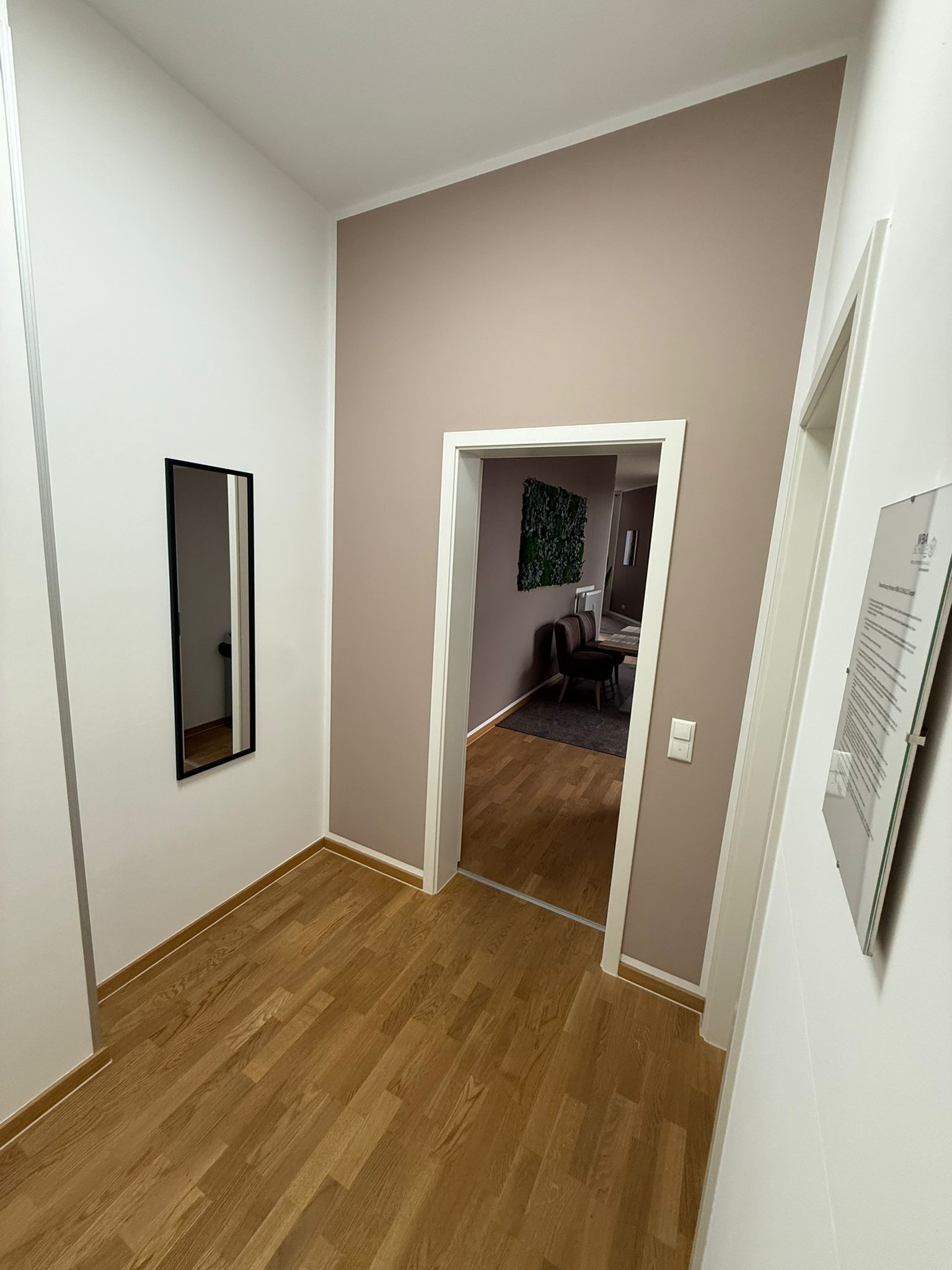Ein Korridor mit Holzboden, einer Tür zu einem Zimmer mit Schreibtisch und Stuhl sowie einem an der Wand befestigten Spiegel.