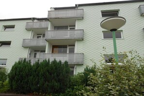 Ein mehrgeschossiges Wohngebäude mit Balkonen, einer Straßenlaterne und dichtem Gebüsch davor.