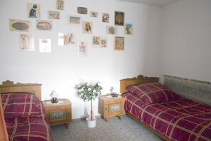 Ein Schlafzimmer mit zwei Betten, einem Nachttisch mit Lampe, einem kleinen Tisch mit Pflanze und einer Wand mit verschiedenen gerahmten Bildern.