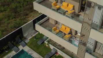 A multi-level residential building with a glass balcony, outdoor seating, and a swimming pool.