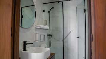 Casa de banho moderna com chuveiro em cabine de vidro, lavatório branco e espelho.