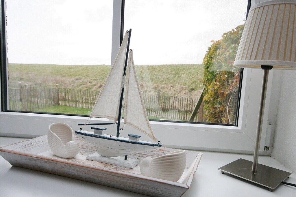 A model sailboat on a tray, a lamp, and a window with a view of a grassy field.