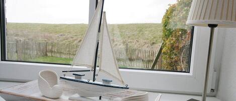 A model sailboat on a tray, a lamp, and a window with a view of a grassy field.