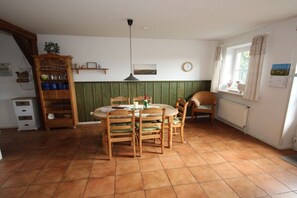 A dining area with a round table, chairs, a hanging light fixture, and a window with curtains. - Holiday apartment with 3 bedrooms (Tönning)
