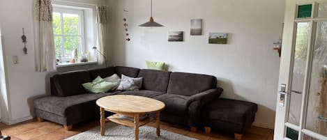 A living room with a sectional sofa, a round coffee table, and a window with curtains.