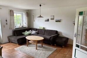 Ein Wohnzimmer mit einer Eckcouch, einem runden Couchtisch und einem fenster mit Vorhängen.