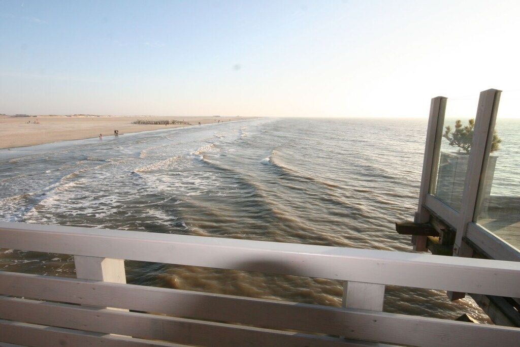 A beach view from a wooden deck with a railing, ocean waves, and a distant shoreline.