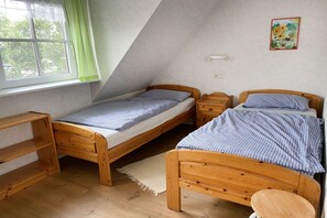Ein kleines Zimmer mit zwei Holzbetten, einem mit Vorhängen versehenen Fenster, einem Regal und einer Wandleuchte.