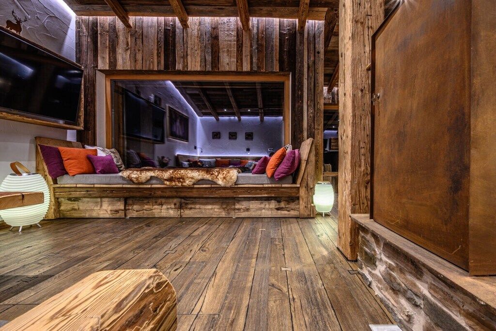 A rustic interior with a wooden bench, a television, and a large wooden door.