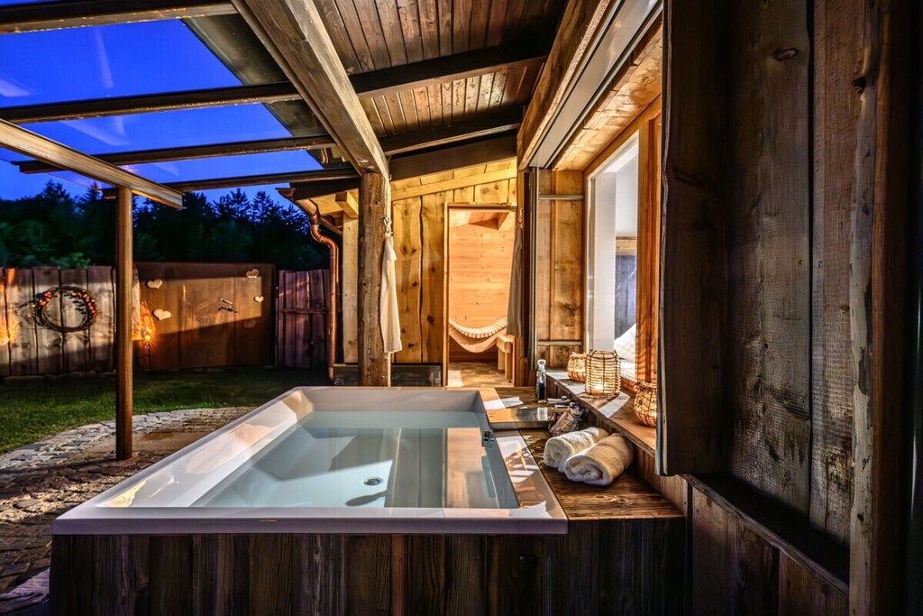 Un espace de détente en bois comprenant un bain à remous, des bancs en bois et un espace extérieur aménagé et abrité.