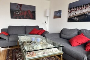 A living room with a grey sofa, red cushions, a glass coffee table with seashells, and two wall-mounted paintings. - Holiday apartment with 2 bedrooms (Wangerland)