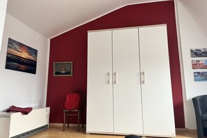 A room with a red wall, a white wardrobe, a radiator, and a chair. - Holiday apartment with 2 bedrooms (Wangerland)