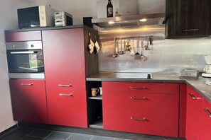 A modern kitchen with stainless steel appliances, red cabinetry, and hanging utensils. - Holiday apartment with 2 bedrooms (Wangerland)