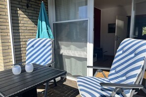 A patio area with a table, two striped lounge chairs, and a sliding glass door leading to an indoor space. - Holiday apartment with 2 bedrooms (Wangerland)