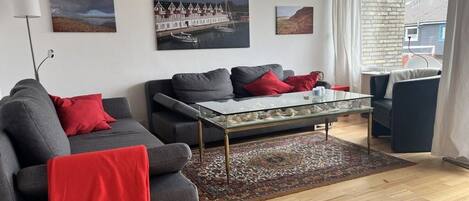 A living room with a sofa, a glass coffee table, and a patterned rug.
