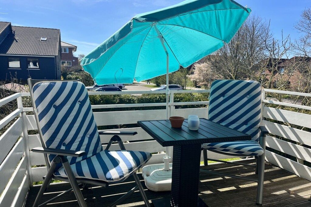 Een terras met twee gestreepte stoelen, een tafel en een turquoise parasol.