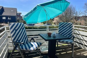A deck with two striped chairs, a table, and a turquoise umbrella. - Holiday apartment with 2 bedrooms (Wangerland)