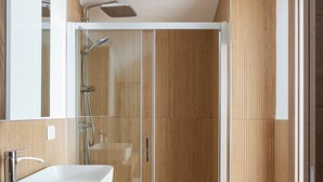 Ein modernes Badezimmer mit einem großen, weißen Waschbecken, einer Duschkabine aus Glas und Holzverkleidung.
