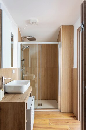 Un bagno moderno con un ampio lavandino bianco, cabina doccia in vetro e rivestimento in legno.
