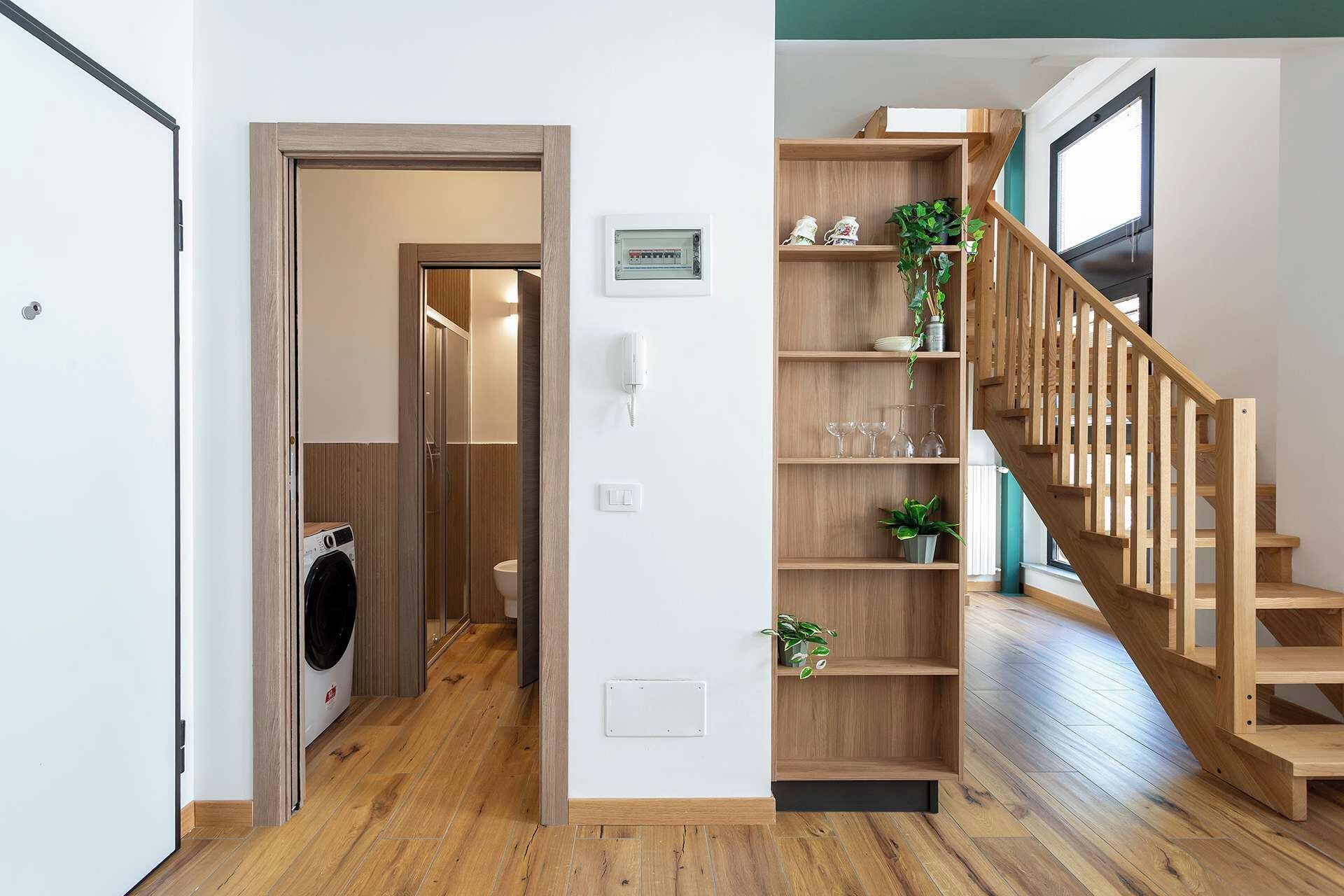 Un interno moderno con una scala in legno, una lavanderia e uno scaffale con oggetti decorativi.