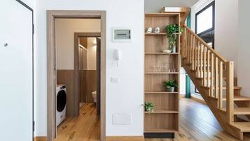 Un interno moderno con una scala in legno, una lavanderia e uno scaffale con oggetti decorativi.