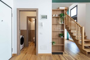 Un interno moderno con una scala in legno, una lavanderia e uno scaffale con oggetti decorativi.