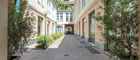 A narrow, paved corridor with buildings on either side, lined with small trees and street lamps.