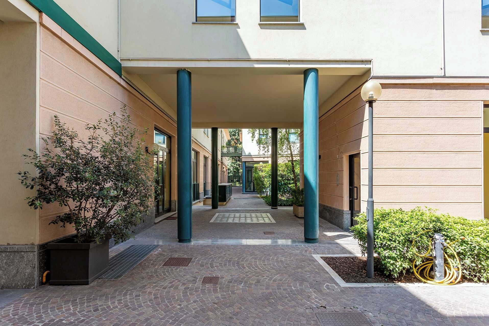 Un porticato con colonne, piante in vaso e un vialetto lastricato che conduce all'ingresso di un edificio.