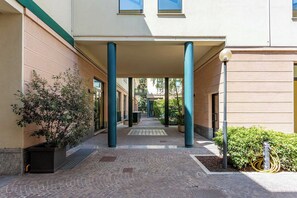Un porticato con colonne, piante in vaso e un vialetto lastricato che conduce all'ingresso di un edificio.