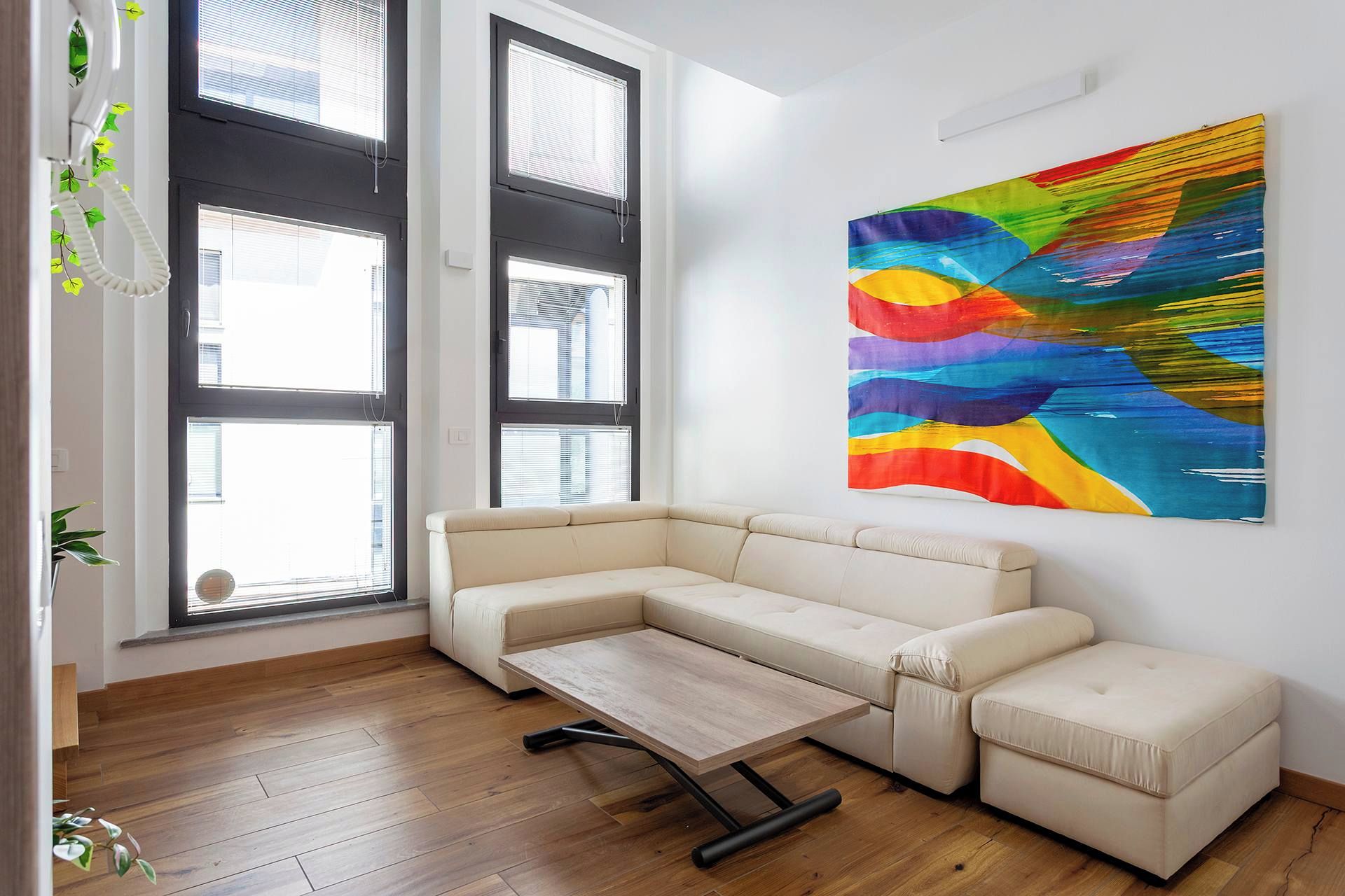 Un soggiorno moderno con un divano angolare beige, un tavolino in legno e un dipinto astratto colorato appeso alla parete.