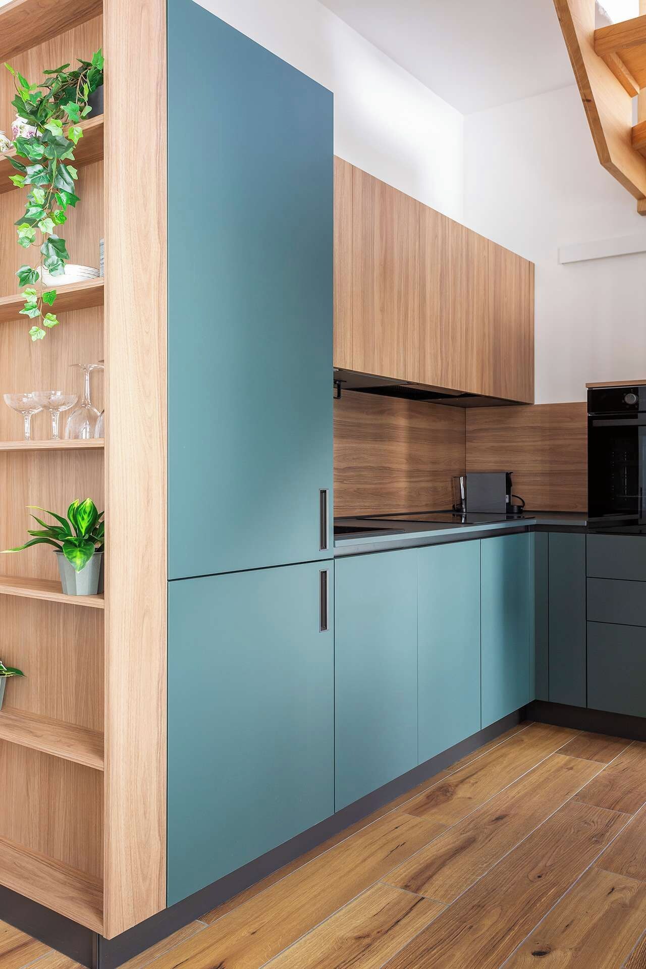 Una cucina moderna con mobili in legno, un piano di lavoro color petrolio e un forno nero.