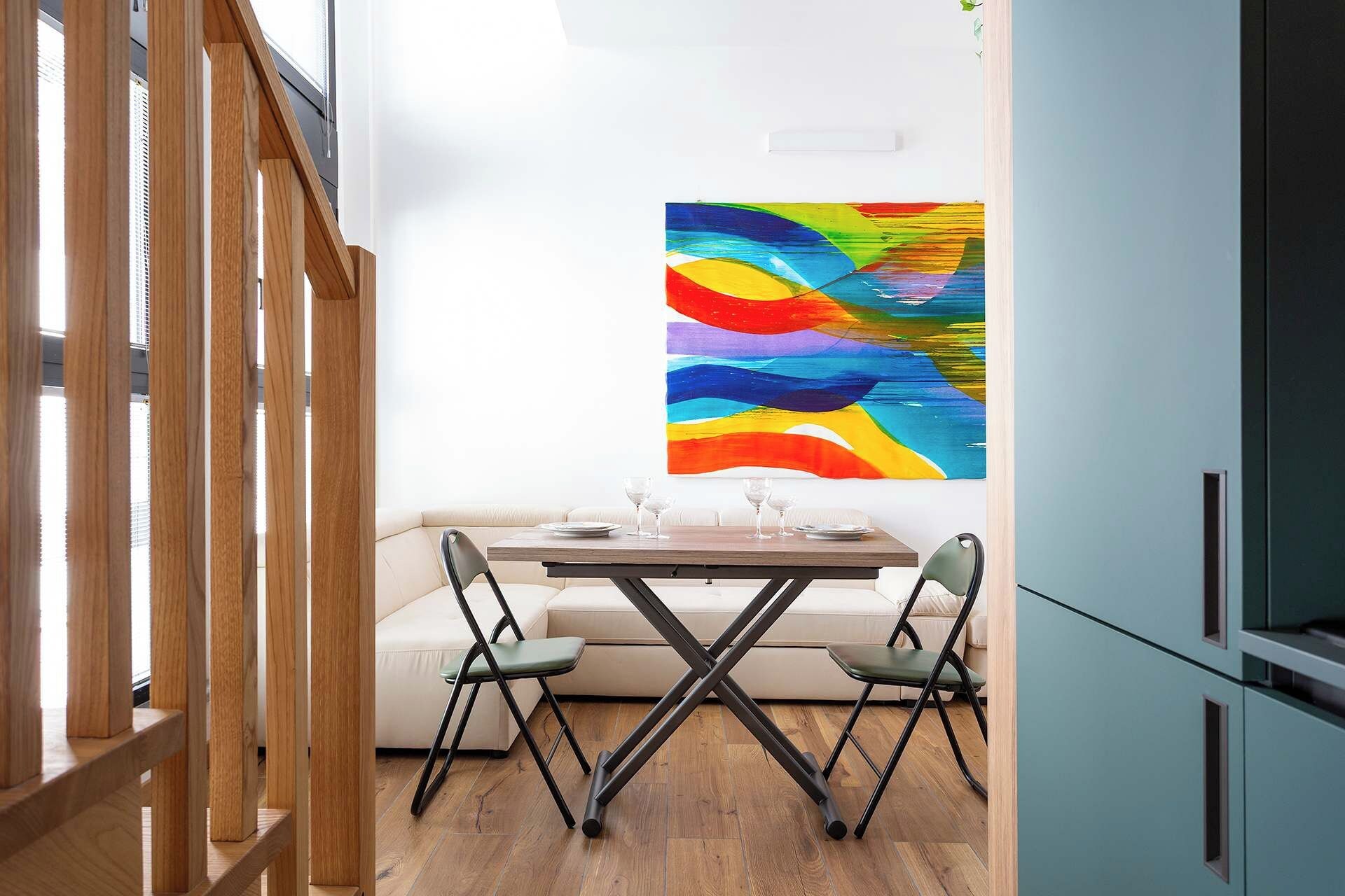 Un'area pranzo con tavolo e sedie, un quadro astratto dai colori vivaci sulla parete e una ringhiera in legno.