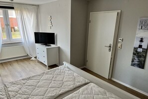 Une chambre à coucher avec un lit, un téléviseur posé sur une commode, une porte et une fenêtre avec des rideaux.