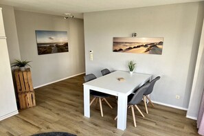 A dining area with a white table and grey chairs, a potted plant, and two landscape paintings on the walls. - Holiday apartment with 1 bedroom (Cuxhaven)