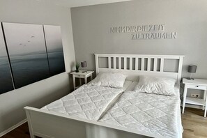 A bedroom with a white bed, two bedside tables, and a wall-mounted artwork. - Holiday apartment with 1 bedroom (Cuxhaven)