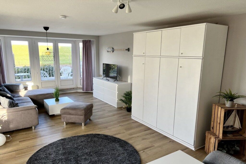 Ein modernes Wohnzimmer mit einer Couch, einem Hocker, einem Couchtisch und einem großen weißen Kleiderschrank.