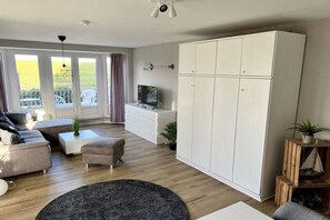 A modern living room with a sofa, ottoman, coffee table, and a large white wardrobe. - Holiday apartment with 1 bedroom (Cuxhaven)